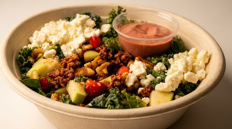 Kale salad with crumbled feta, ground meat, apples, walnuts, and a side of dressing.