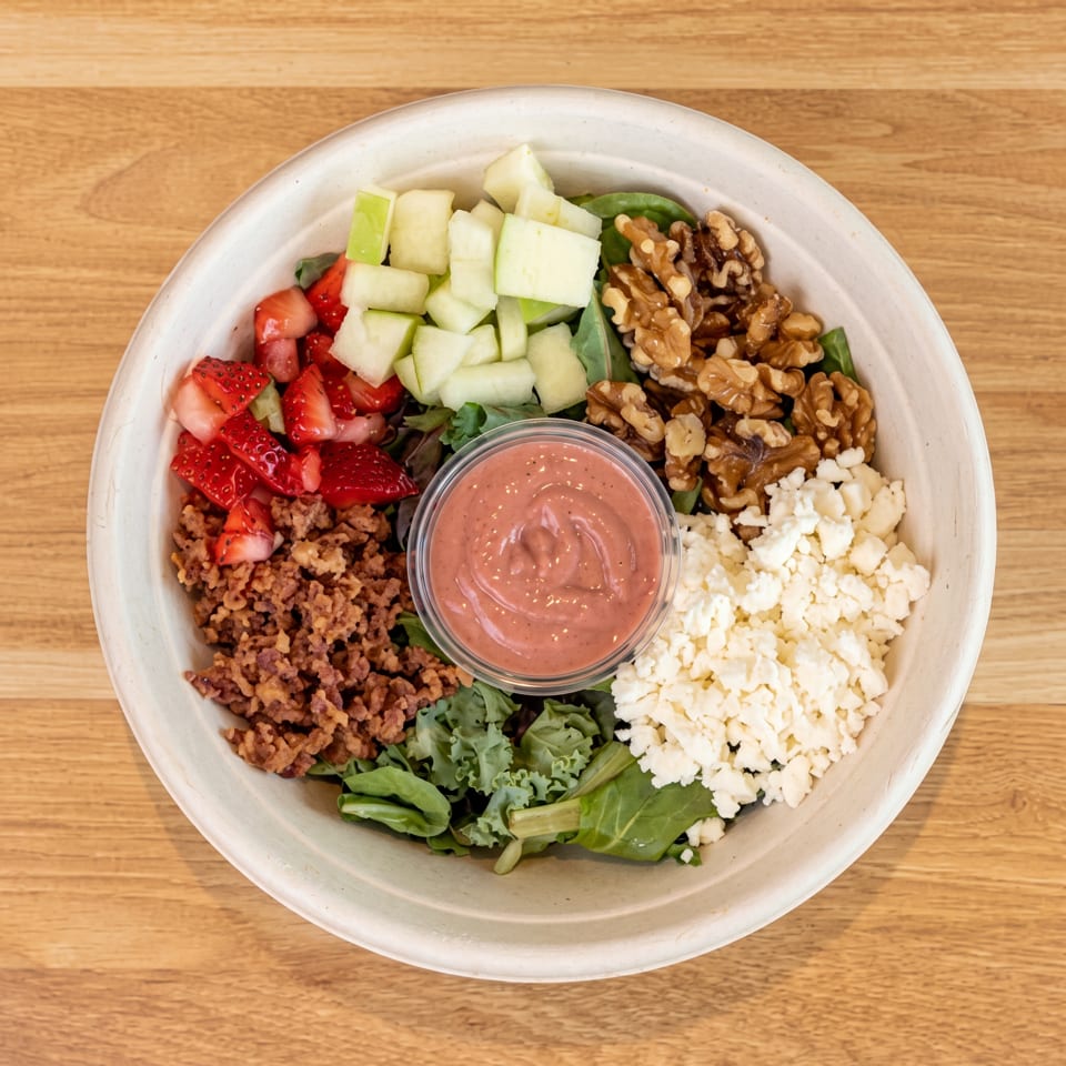 Vibrant salad bowl with strawberries, green apples, walnuts, crumbled cheese, and pink dressing.