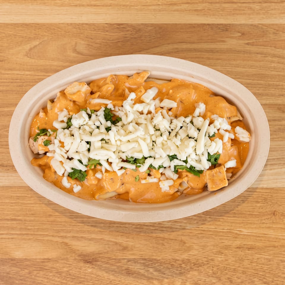 Creamy orange chicken dish topped with shredded cheese and fresh herbs in a takeout bowl.