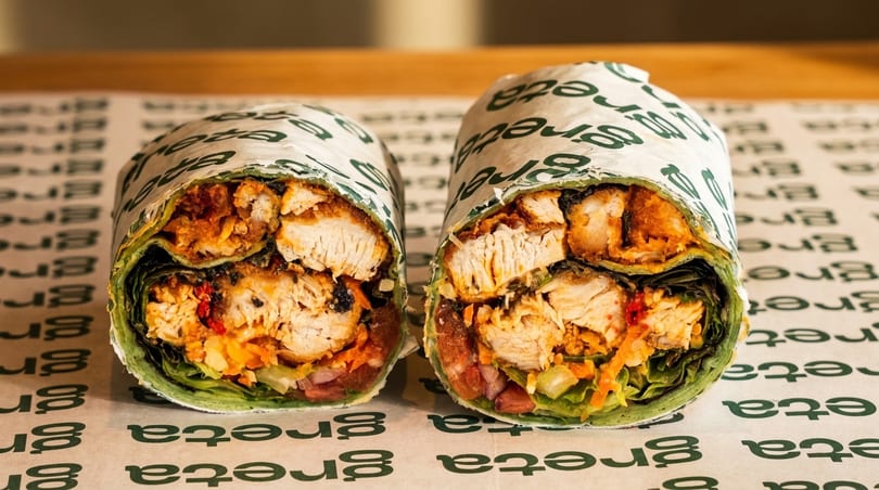 Two halves of a chicken wrap, filled with lettuce, vegetables, and sauce, on branded paper.