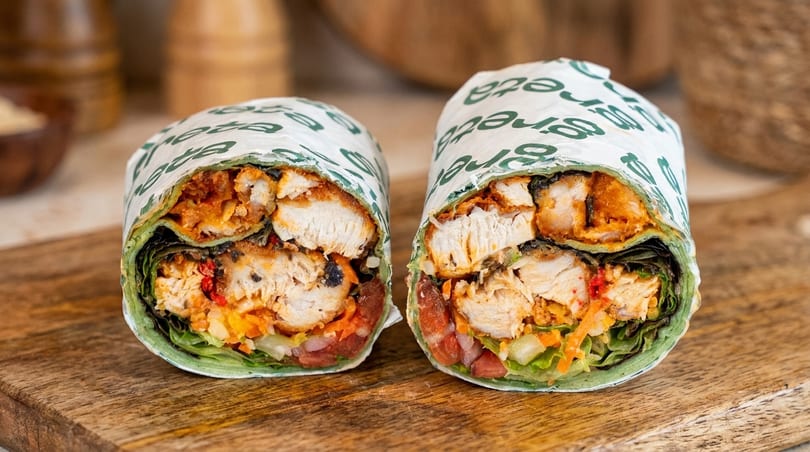 Two halves of a chicken wrap with lettuce, carrots, and red peppers on a wooden board.