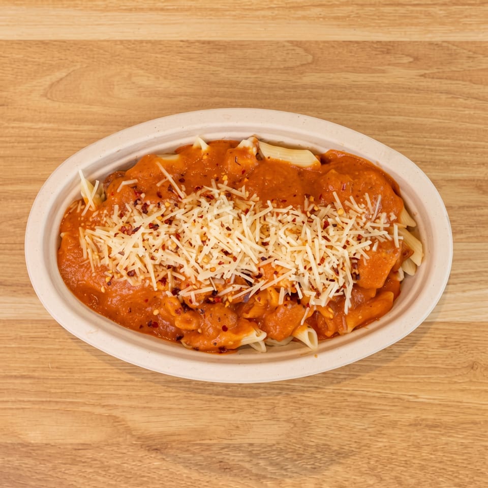Penne pasta with tomato sauce, parmesan cheese, and chili flakes in an oval bowl on a wooden surface.