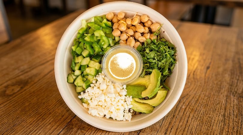 A colorful salad bowl with chickpeas, avocado, feta, bell peppers, cilantro, and dressing.