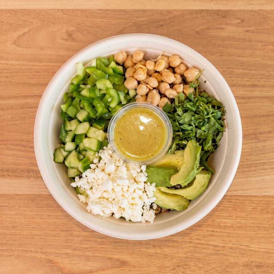 Overhead view of a healthy bowl with chickpeas, avocado, feta, green peppers, and dressing.