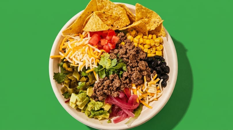 Overhead view of a taco bowl with ground beef, cheese, corn, black beans, avocado, and tortilla chips.