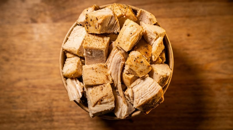 Close-up overhead view of a bowl filled with diced, seasoned chicken pieces on a wooden surface.